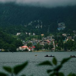 Picturesque landscape of Nainital Lake with misty mountains and lush greenery.